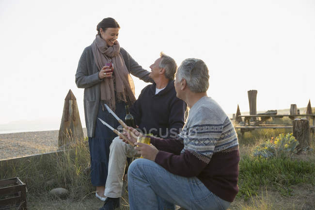 Mature friends barbecuing and drinking wine on sunset beach — Stock Photo