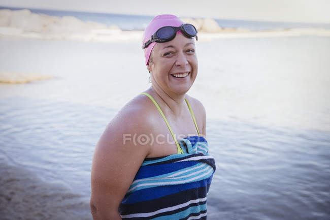 Портрет усміхненого плавця відкритої води, загорнутого в рушник на океанічному пляжі — стокове фото