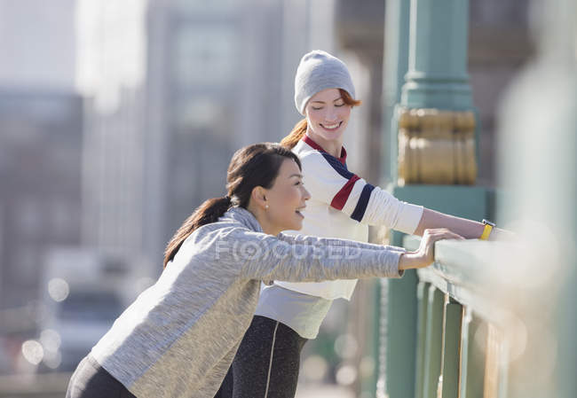 Усміхнені жінки бігуни тягнуться і розмовляють на сонячних міських перилах — стокове фото