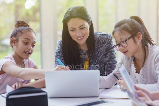 Female teacher and girl students researching at laptop in library — Stock Photo