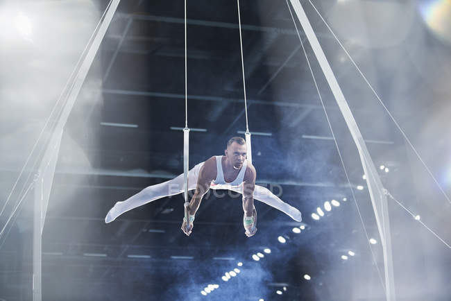 Male gymnast performing on gymnastics rings in arena — Stock Photo