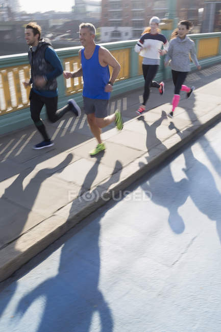 Runners running on sunny urban bridge sidewalk — Stock Photo