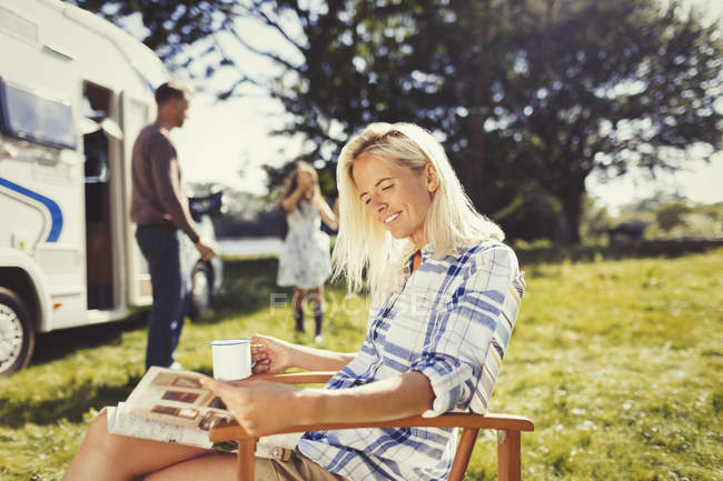 Woman reading magazine and drinking coffee outside sunny motor home — Stock Photo