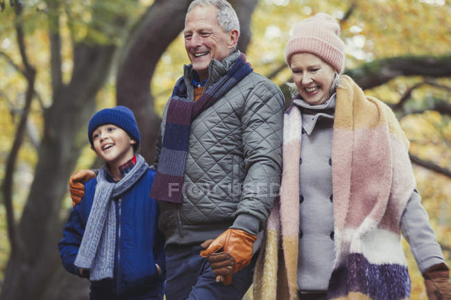 Бабушка и дедушка, гуляющие с внуком в осеннем парке — стоковое фото