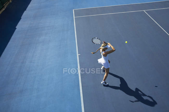 Молодая теннисистка, играющая в теннис на солнечном синем теннисном корте — стоковое фото