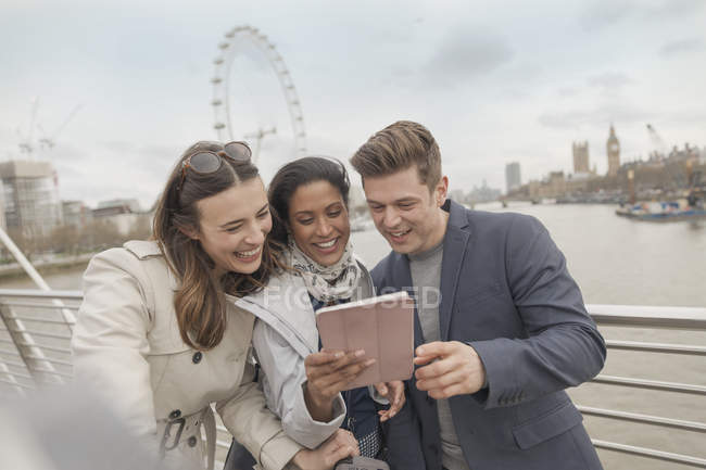 Friend tourists using digital tablet on bridge over Thames River, London, UK — Stock Photo