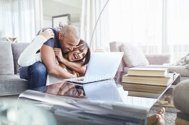 Verspieltes Paar umarmt und benutzt Laptop im Wohnzimmer — Stockfoto