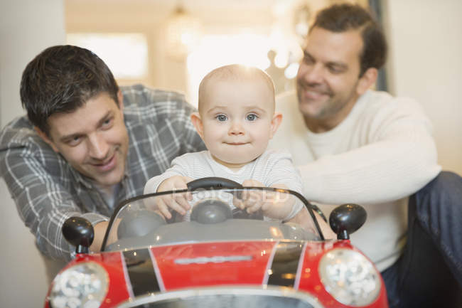 Portrait mâle gay parents poussant bébé fils dans jouet voiture — Photo de stock