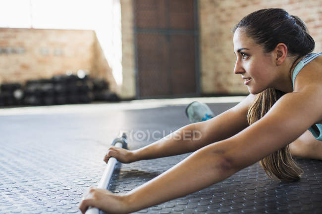 Jovem mulher se alongando com barra no ginásio — Fotografia de Stock