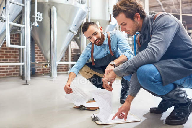 Male brewers with clipboard near vat in brewery — Stock Photo