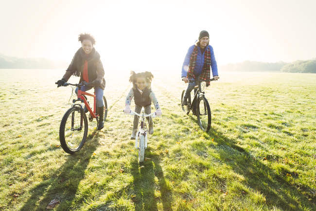 Portrait young family bike riding in sunny autumn park grass — Stock Photo
