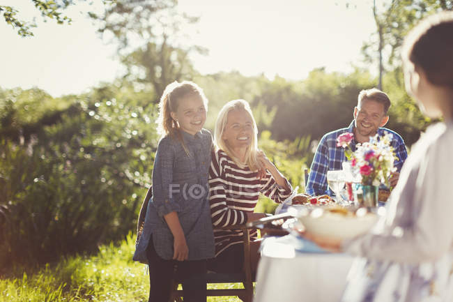 Счастливая семья, наслаждающаяся обедом в солнечном саду за столом во внутреннем дворике — стоковое фото