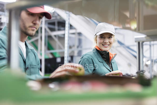 Портрет улыбающейся женщины, осматривающей яблоки на заводе по переработке пищевых продуктов — стоковое фото
