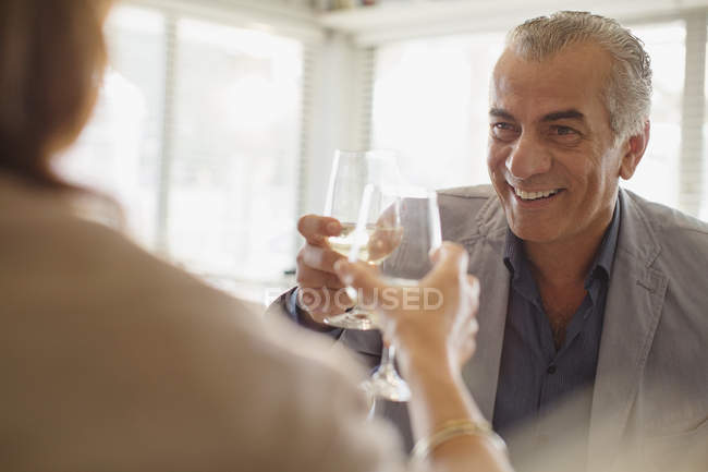 Улыбающийся пожилой мужчина пьет вино, пьет бокалы с женщиной в ресторане — стоковое фото