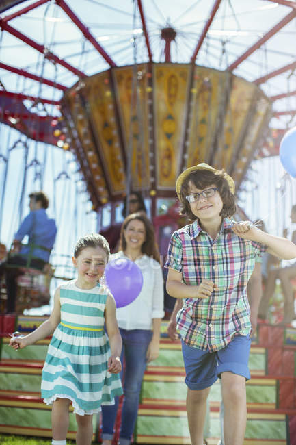 Children running in front of carousel, mother following them — Stock Photo