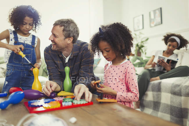 Многонациональный отец и дочери играют в игрушки в гостиной — стоковое фото