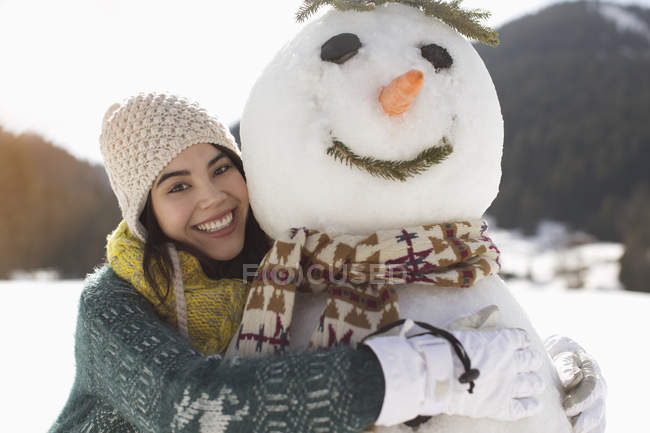 Portrait of smiling woman hugging snowman — Stock Photo