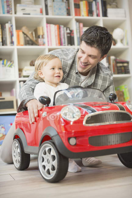 Отец толкает маленького сына в игрушечной машине — стоковое фото