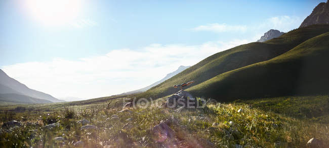 Молодий чоловік робить горизонтальну сумочку на скелі в сонячній, віддаленій долині — стокове фото