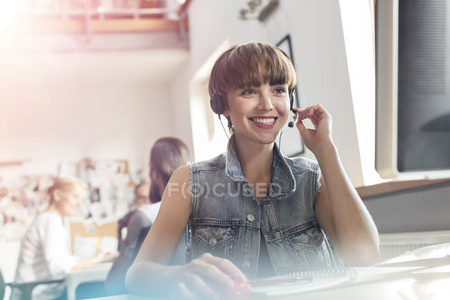 Profissional de design sorridente usando fone de ouvido com microfone no escritório — Fotografia de Stock