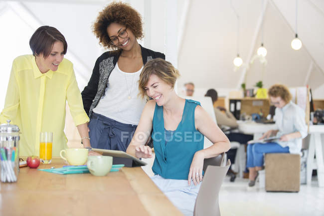 Жінки дивляться на цифровий планшет і посміхаються в офісі — стокове фото