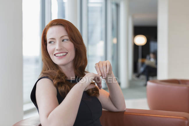 Femme d'affaires souriante aux cheveux roux regardant par-dessus l'épaule dans le salon — Photo de stock