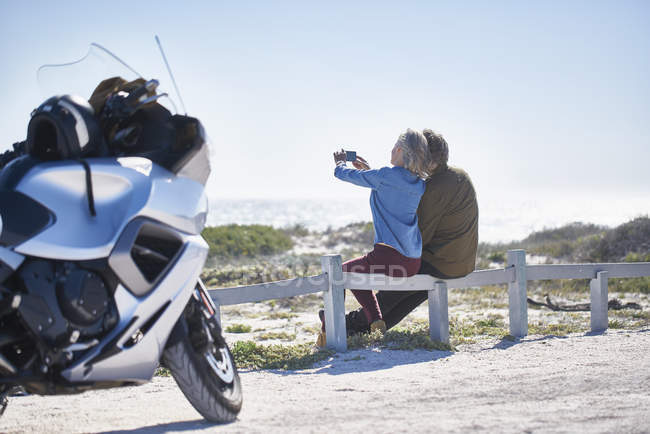 Senior couple taking selfie at sunny roadside near motorcycle — Stock Photo