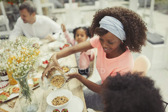 Mother pouring granola cereal for daughter at breakfast table — Stock Photo