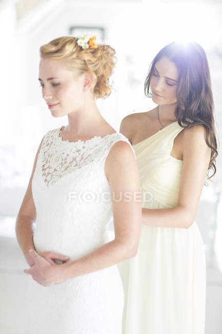 Bridesmaid helping bride with dressing in bedroom — Stock Photo