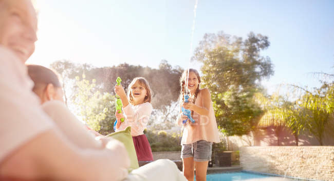 Playful sisters with squirt guns spraying water at sunny summer poolside — Stock Photo