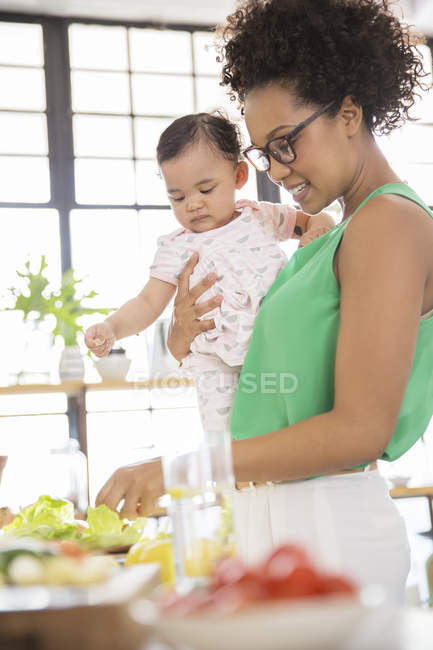 Женщина с малышкой готовит еду на домашней кухне — стоковое фото