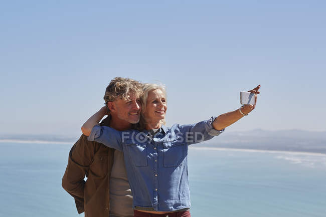 Affectionate senior couple taking selfie overlooking sunny ocean view — Stock Photo