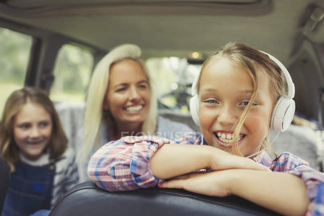 Ritratto sorridente ragazza con le cuffie sul sedile posteriore della macchina — Foto stock