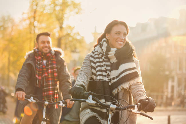 Sonriente joven pareja bicicleta a caballo en la calle urbana de otoño - foto de stock