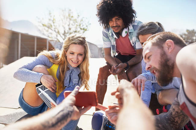 Personal perspective man showing friends video on smart phone at sunny skate park — Stock Photo