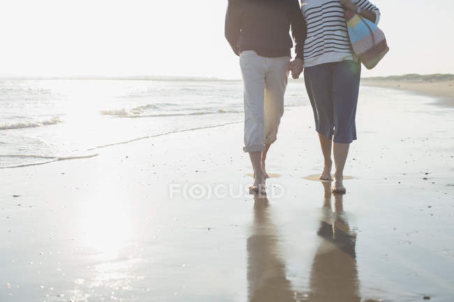 Cariñosa pareja madura descalza caminando, tomados de la mano en el sol mar playa surf - foto de stock
