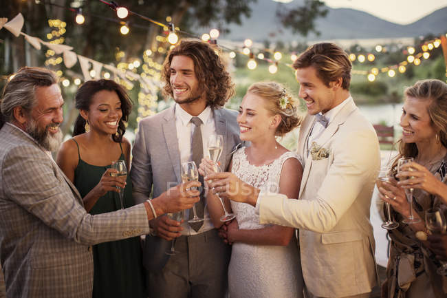 Молодая пара и их гости с шампанским флейты во время свадебного приема в саду — стоковое фото