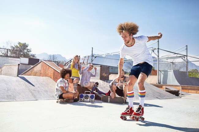 Freunde beobachten Mann beim Rollschuhlaufen im sonnigen Skatepark — Stockfoto