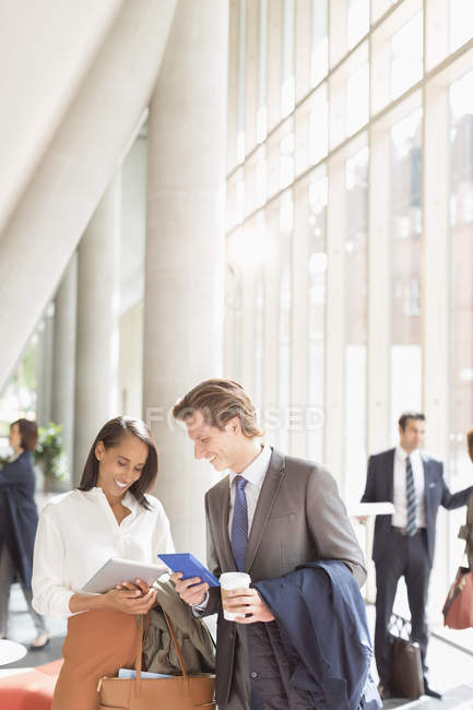 Business people using digital tablets talking in sunny office lobby — Stock Photo