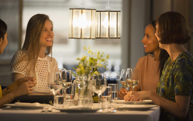 Lächelnde Freundinnen essen und trinken Wein am Restauranttisch — Stockfoto