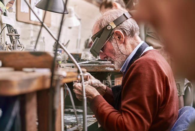 Jeweler wearing headband magnifier working in workshop — Stock Photo