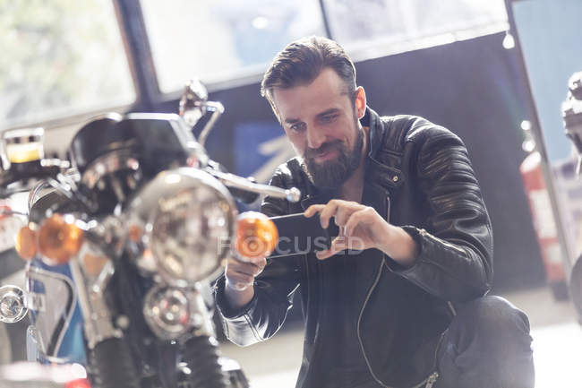 Man with camera phone photographing motorcycle in shop — Stock Photo