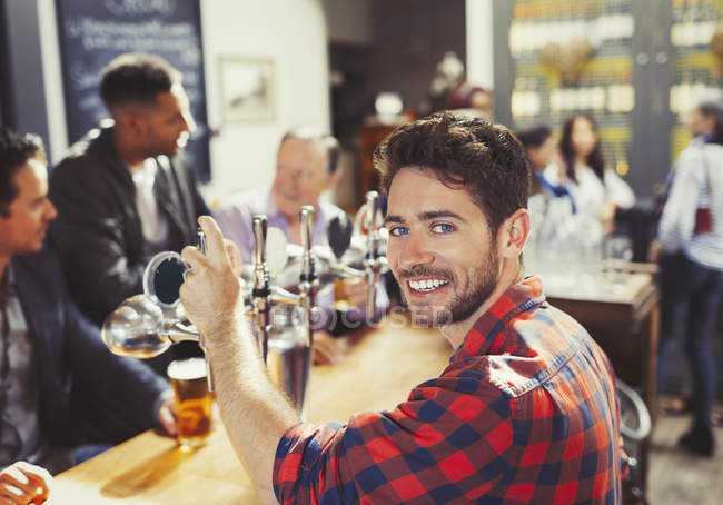 Retrato sonriente, confiado camarero masculino sirviendo cerveza en el bar - foto de stock