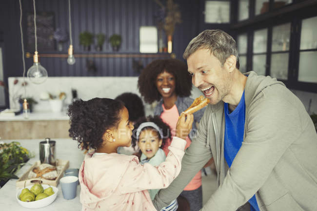 Multi-ethnic daughter feeding toast to father in kitchen — Stock Photo