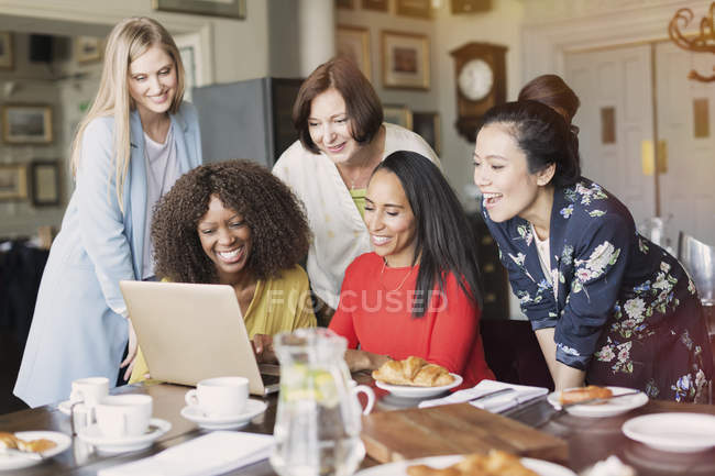 Mujeres sonrientes amigas usando el portátil en la mesa del restaurante - foto de stock