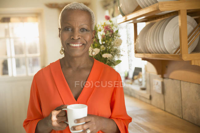Портрет усміхненої старшої жінки, що п'є каву на кухні — стокове фото