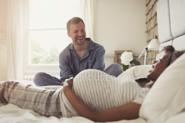 Multi-étnica pareja embarazada relajarse y reír en la cama - foto de stock