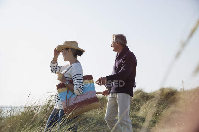 Mature couple walking on sunny beach grass path — Stock Photo