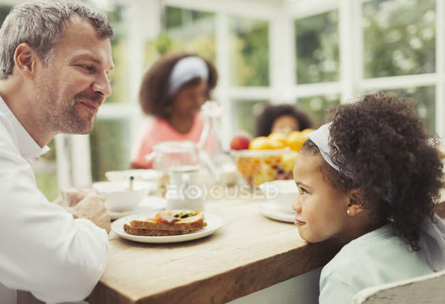 Multi-étnico padre e hija jugando mirando fijamente juego en la mesa de la cocina - foto de stock
