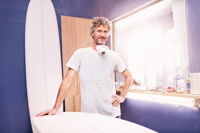 Porträt selbstbewusster männlicher Surfbrettdesigner schleift Surfbrett in Werkstatt — Stockfoto
